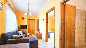 Un salón con sofá, reposapiés, televisión y una mesita con una planta.