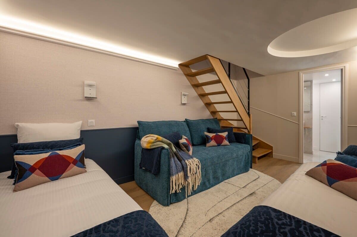 A modern bedroom with a sofa bed, a wooden ladder, and a staircase leading to a door.