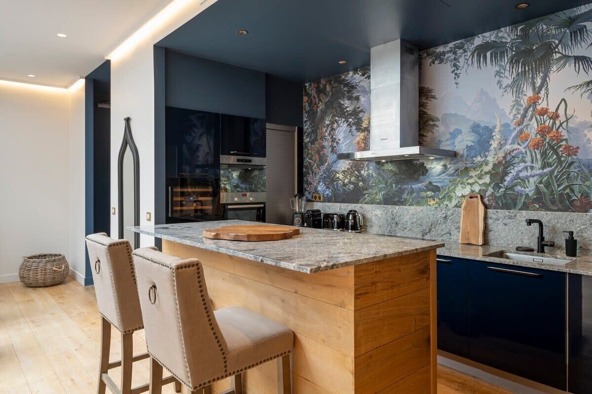 A modern kitchen with a central island, dark cabinetry, and a large mural of a tropical scene.