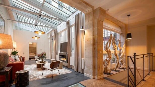 A spacious living area with a high ceiling, a fireplace, and a glass railing overlooking the interior. - L'Atelier des Arts in Paris (Paris)