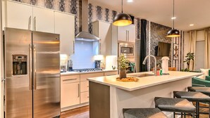 Une cuisine moderne dotée d’appareils électroménagers en acier inoxydable, d’un îlot central avec des tabourets de bar et d’un papier peint à motifs.