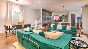 Un salon moderne avec des canapés verts, un coin repas, une cuisine et un escalier.