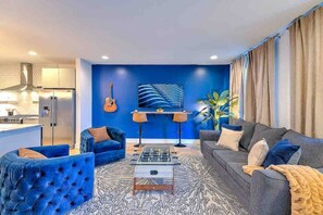 A modern living room with a sofa, armchairs, a coffee table, and a wall-mounted guitar.