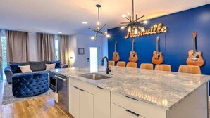 Cozinha moderna com bancada de mármore, pia embutida e área de jantar com parede azul e guitarras.