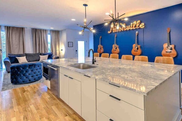 A modern kitchen with a marble countertop, a built-in sink, and a dining area with a blue wall and guitars.