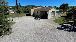 Ein Schotterweg führt zu einem kleinen Gebäude mit Ziegeldach, vor dem ein Fahrrad abgestellt ist, und im Hintergrund ist ein Pool zu sehen.