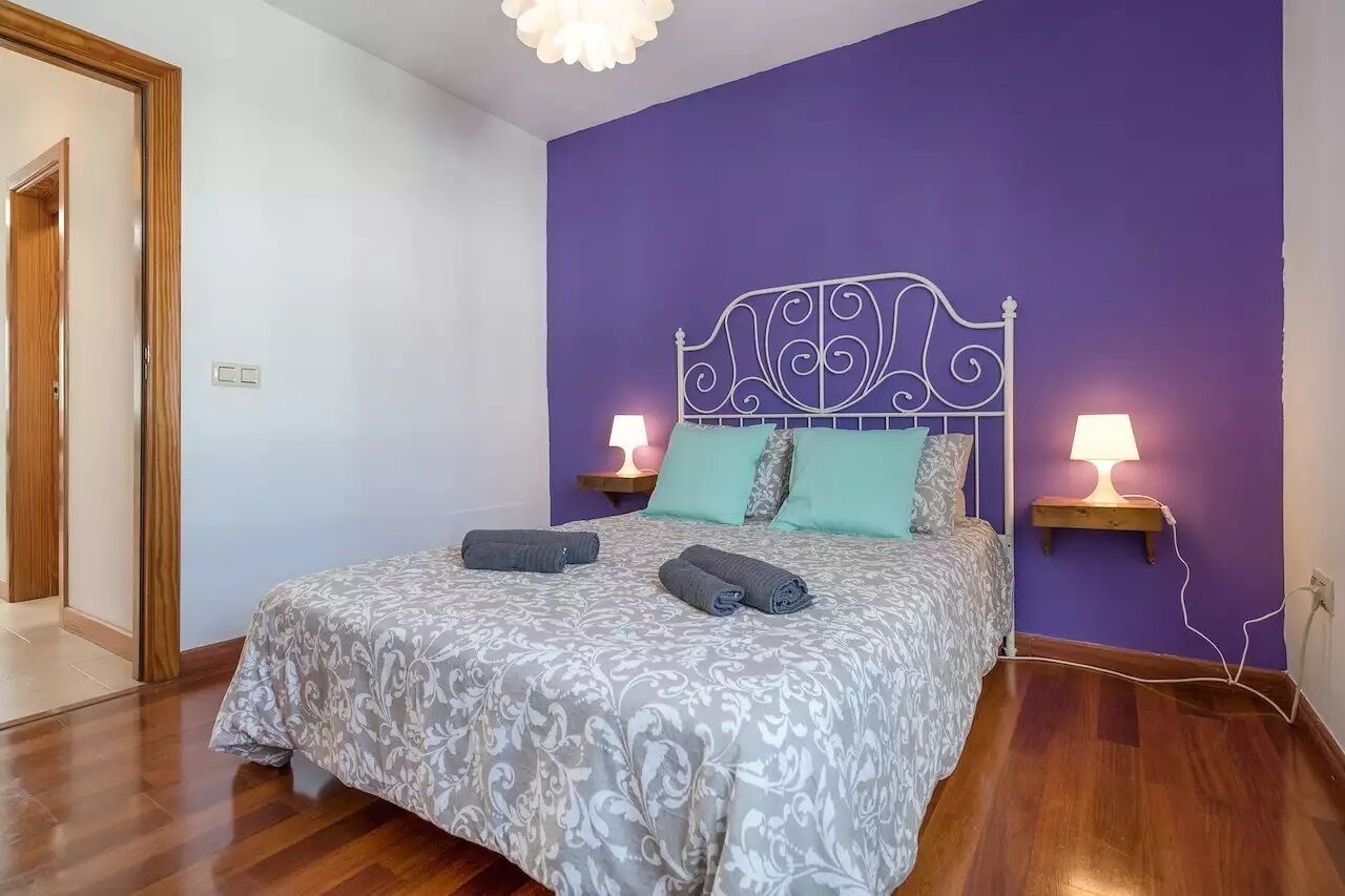 A bedroom with a bed, two bedside lamps, and a purple wall.
