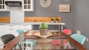 Una cocina moderna con armarios blancos, encimera de madera, mesa de comedor de vidrio y un reloj en la pared.