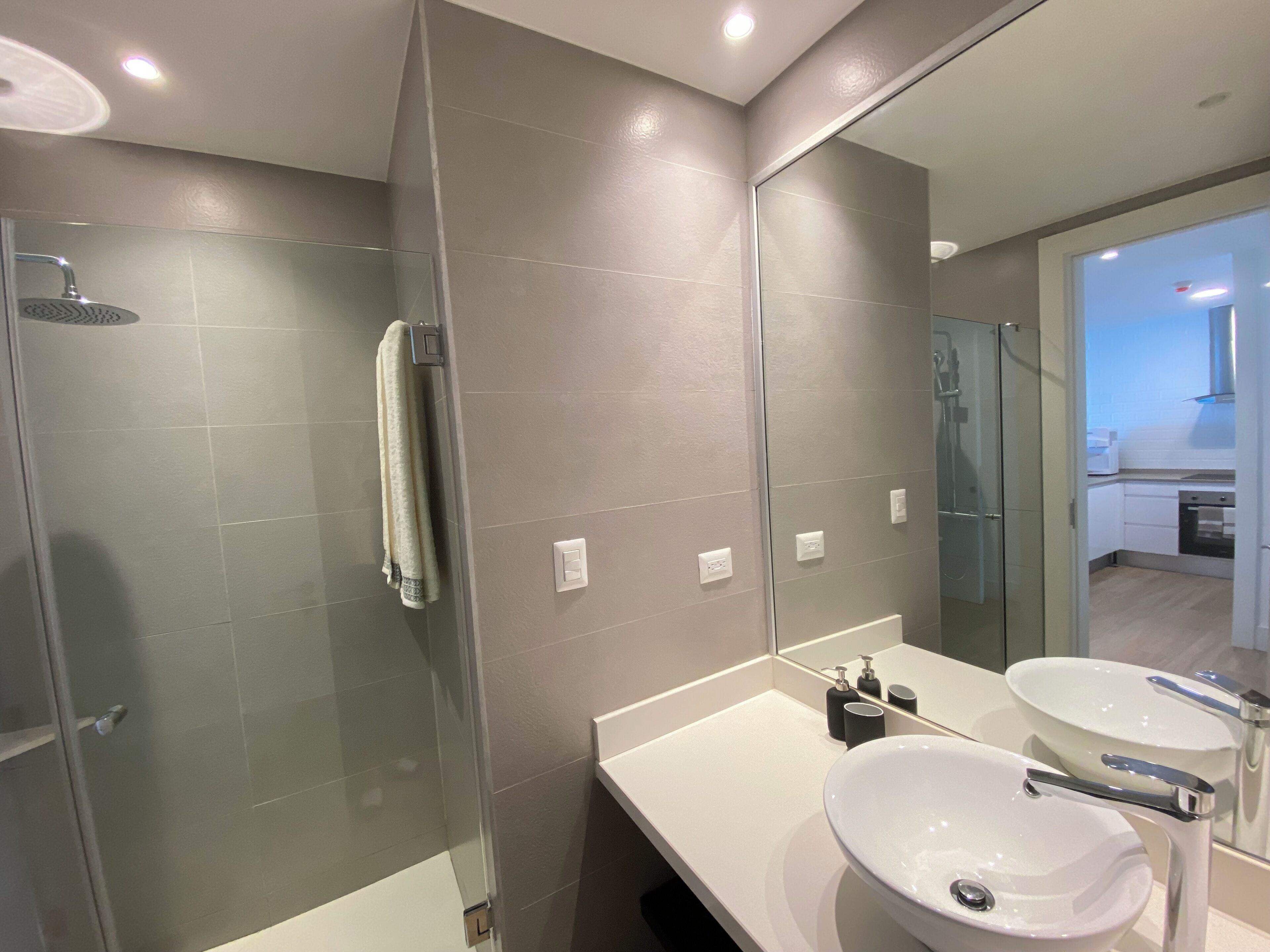A modern bathroom with a glass-enclosed shower, a white sink, and a large mirror.