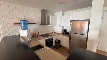 A modern kitchen with white cabinets, a stainless steel refrigerator, a built-in oven, and a coffee maker.