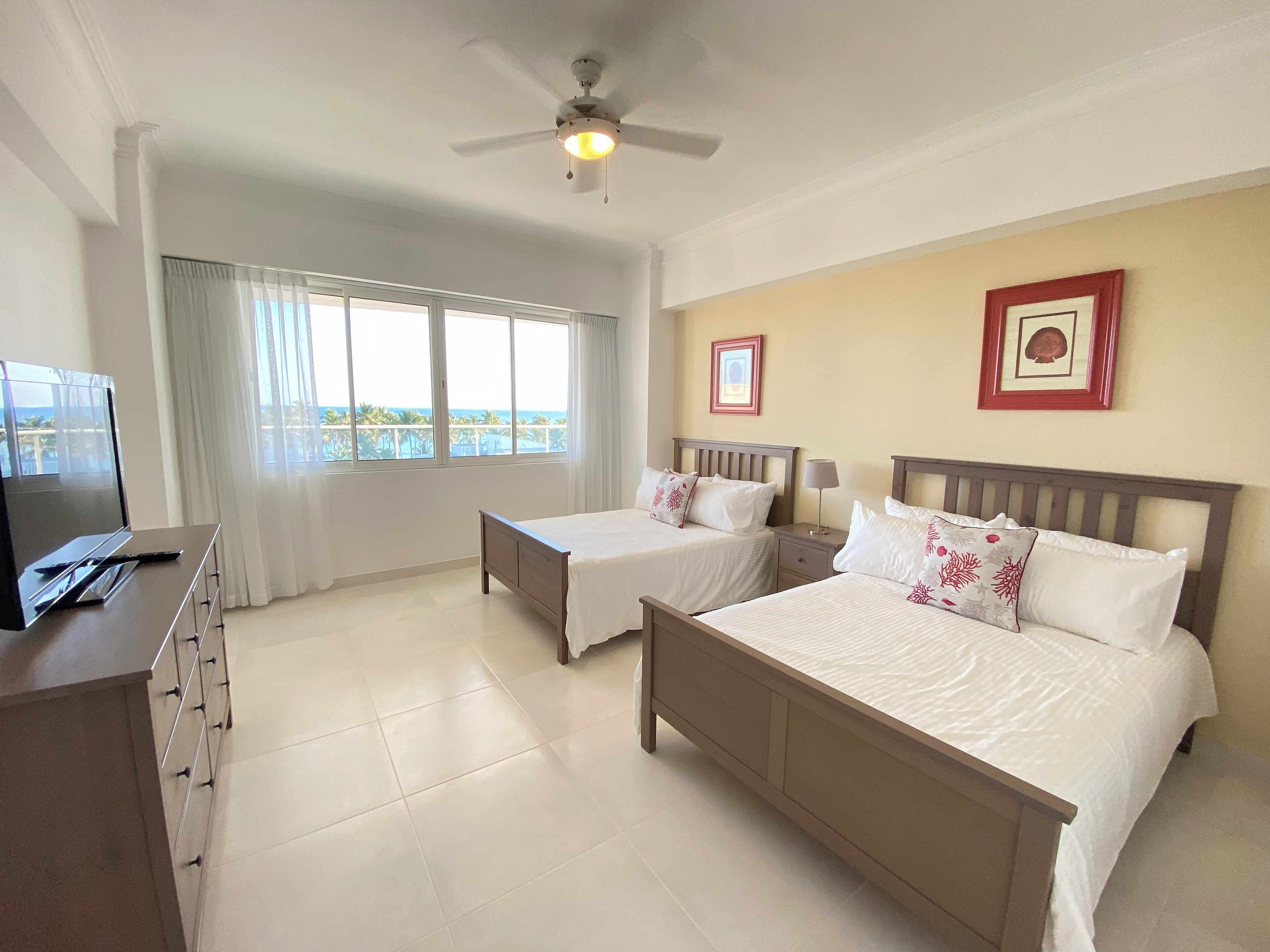 A hotel room with two beds, a TV, a ceiling fan, and a balcony with a view.