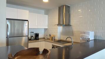 A modern kitchen with stainless steel appliances, a built-in oven, a coffee maker, and a wooden bowl on the counter.