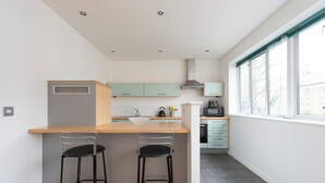 A modern kitchen with a wooden countertop, two black bar stools, a stainless steel range hood, and a window with blinds. - Modern Luxury Appt by Bow Road Station (London)