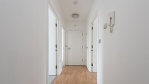 A narrow hallway with wooden flooring, white walls, and a door at the end. - Modern Luxury Appt by Bow Road Station (London)