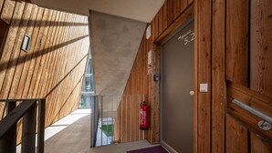 Exterior de madeira com um extintor preso na parede, uma porta com um número e um tapete roxo que leva a uma varanda.