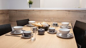 Uma mesa de jantar com tigelas, xícaras e um bule brancos e cinzas, acompanhados por uma cesta de pão.