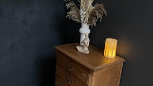 Un aparador de fusta amb calaixos, un vas amb plantes seques i una espelma encès.