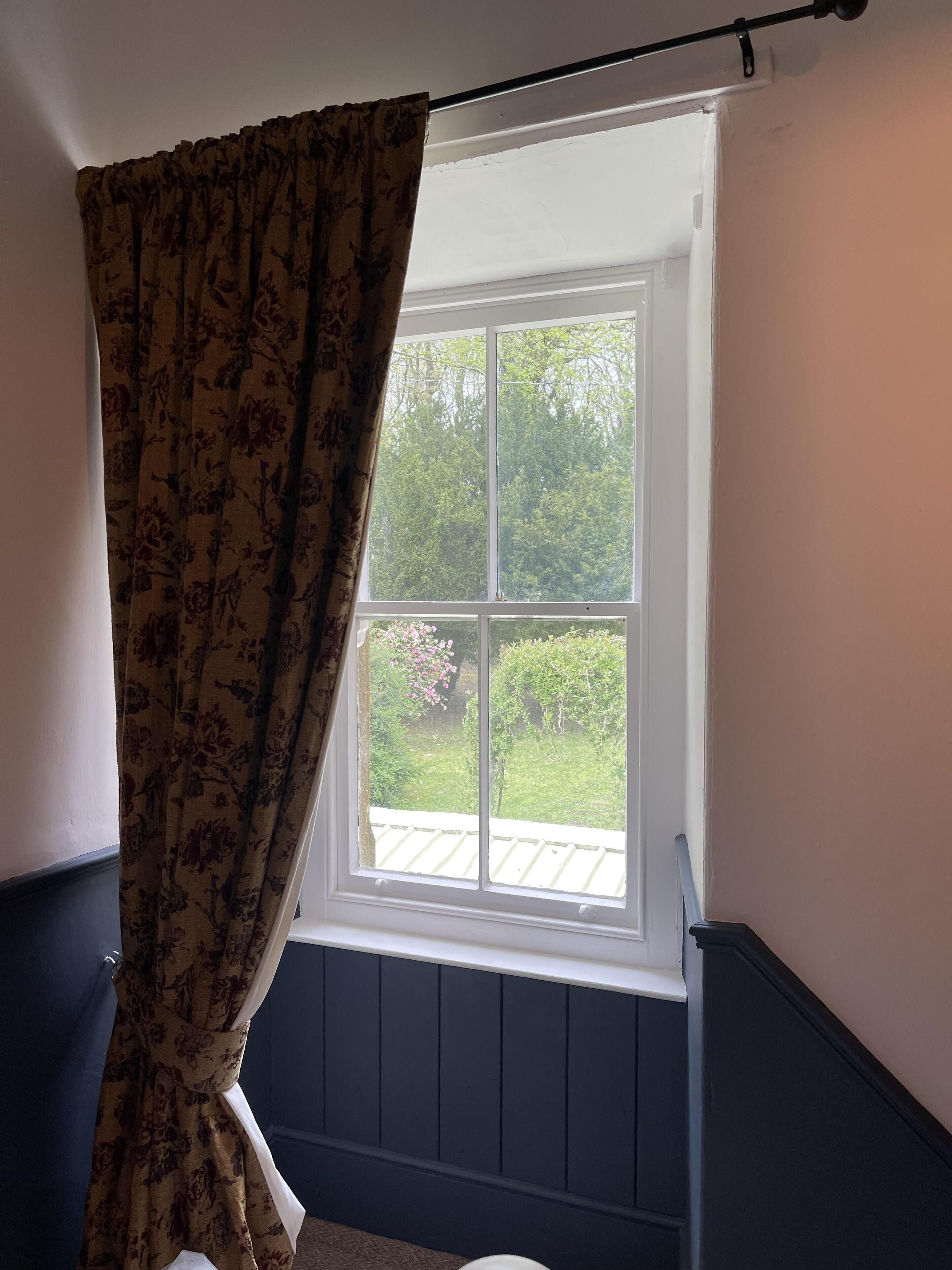 A room with a window, a curtain, and a view of greenery outside.