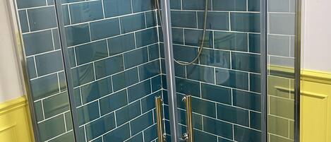 A glass-enclosed shower with a handheld showerhead and a wall-mounted control panel.