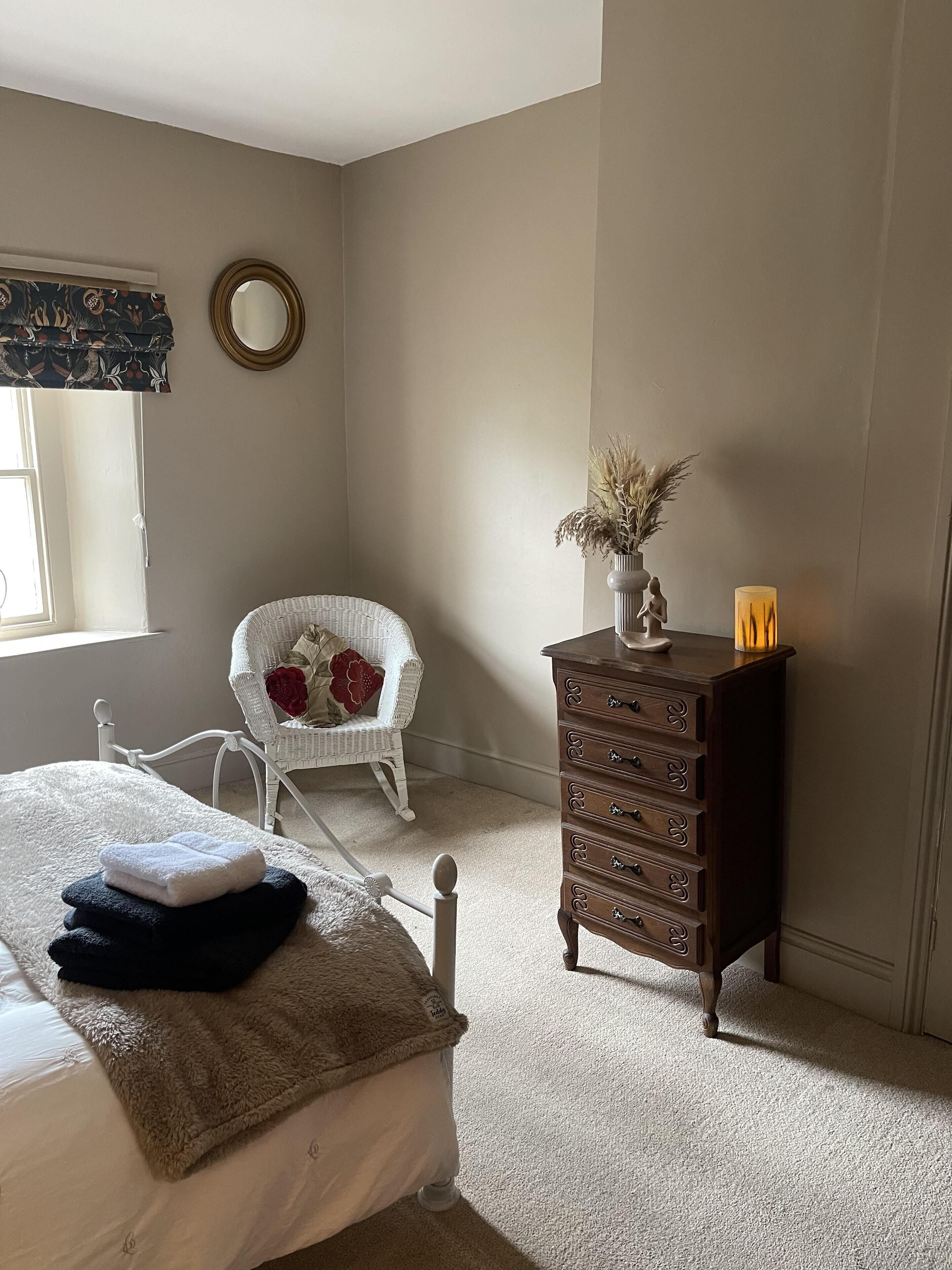 Un dormitorio con cama, cómoda, silla y ventana.