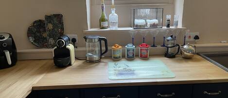 A kitchen with a coffee maker, kettle, sugar, tea, and a teapot on the counter.