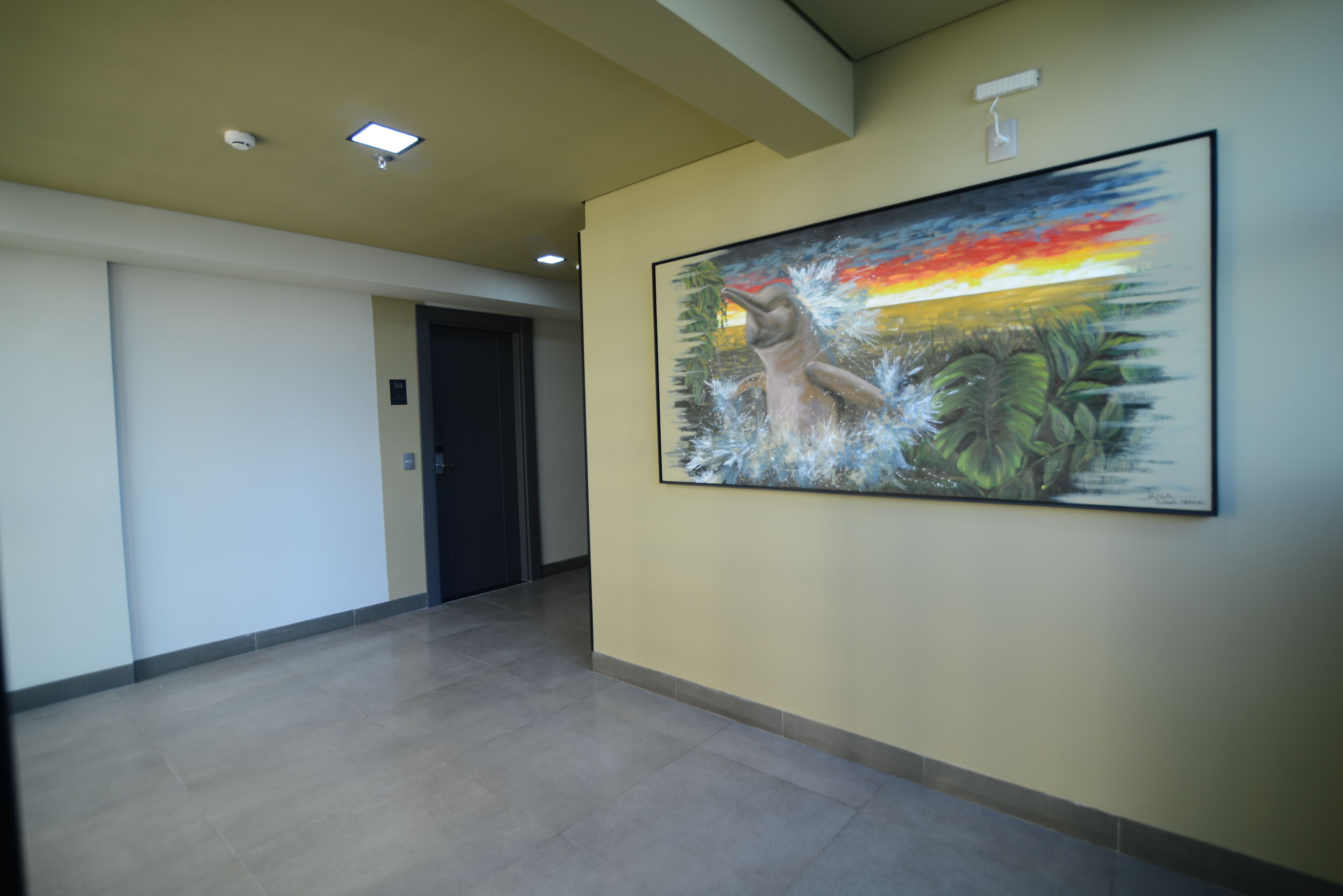 A hallway with a large painting of a dolphin and a sunset, a door, and a ceiling with recessed lighting.