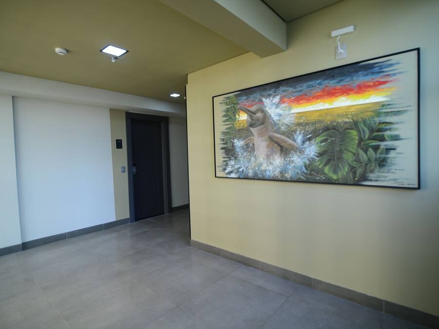 A hallway with a large painting of a dolphin and a sunset, a door, and a ceiling with recessed lighting.