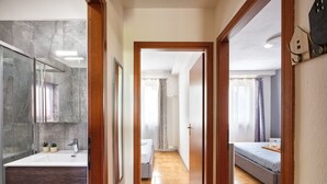 Ein modernes Hotelzimmer mit Bad, einem Flur, der zum Schlafzimmer führt, und einem Essbereich.