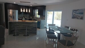 A modern kitchen with a central island, dark cabinetry, and a dining area with a glass table and chairs. - CAPE CORAL FLORIDA DREAM $155  last minute  (Cape Coral)