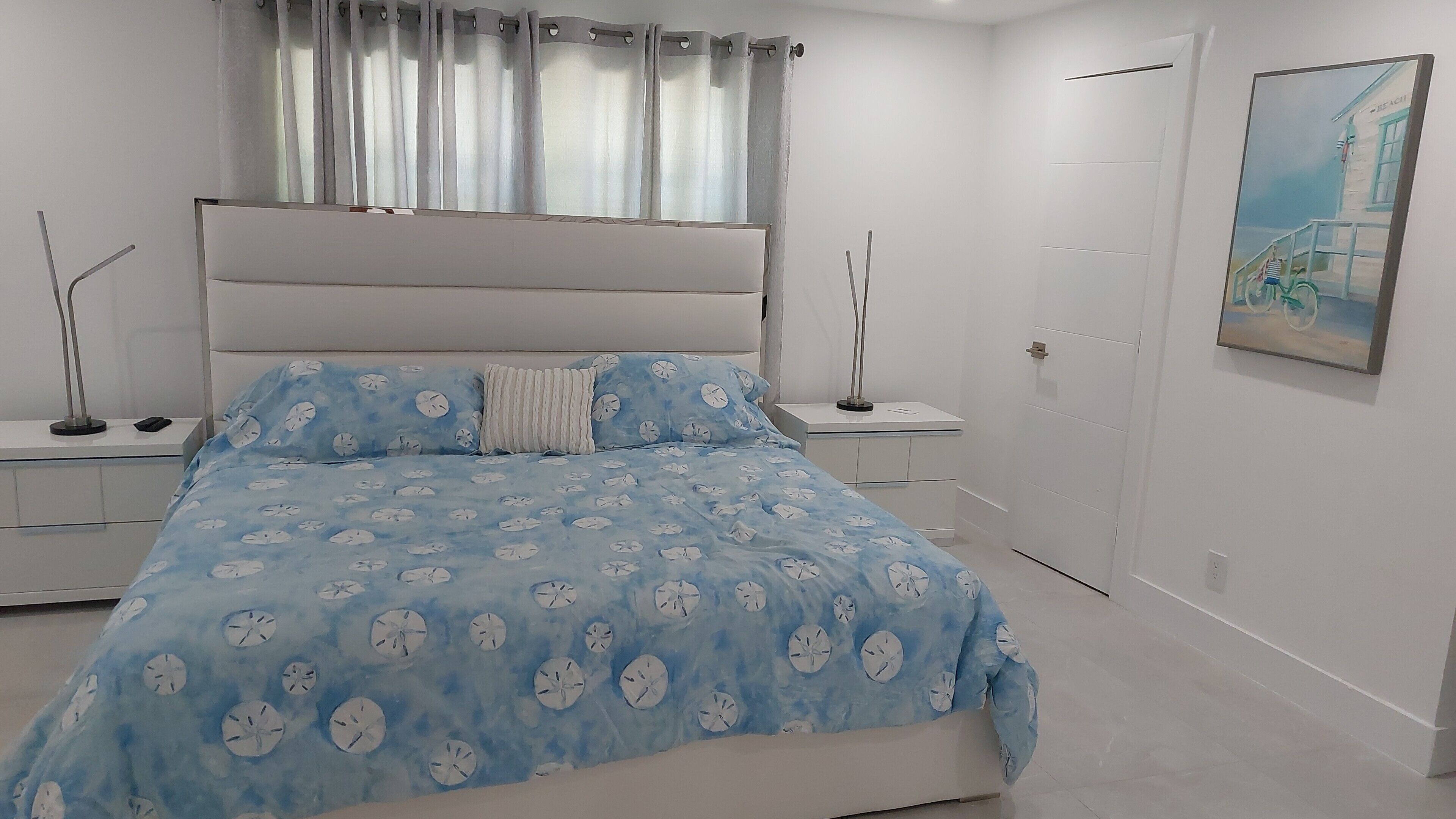 Ein Schlafzimmer mit einem Bett, Nachttischen, einem Gemälde und einer Tür.