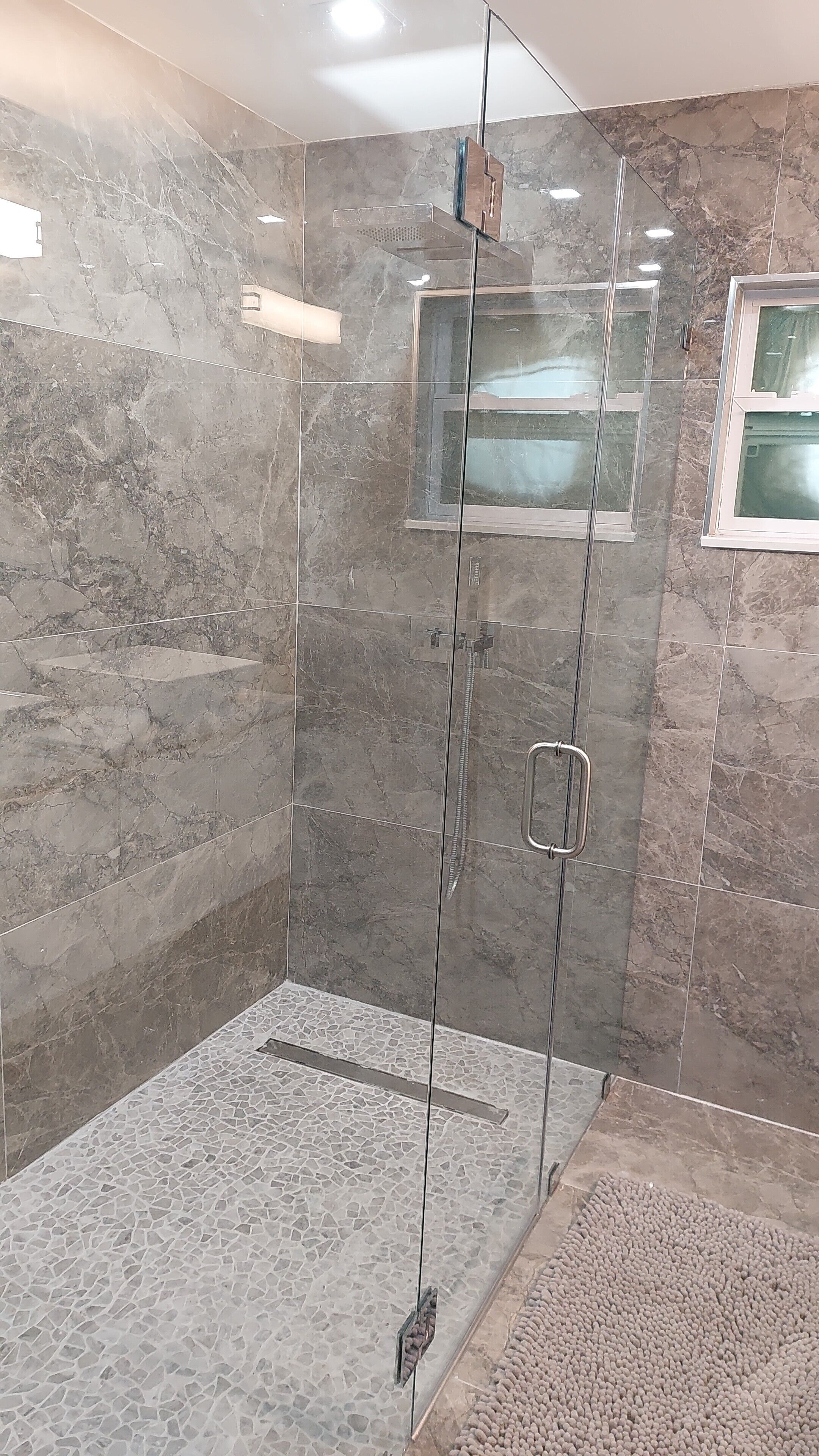 A glass-enclosed shower with a marble wall and a small window.