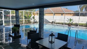 A poolside area with a glass table and chairs, a clear view of the pool, and a white fence in the background. - CAPE CORAL FLORIDA DREAM $155  last minute  (Cape Coral)