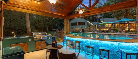 Resort-style evening at Teal Paradise - the lighted pool, swim-up bar, and covered outdoor kitchen create the perfect setting for grilling, relaxing, and spending time together.