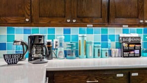 A kitchen with wooden cabinets, a coffee maker, a coffee mug, a water dispenser, a tea kettle, a blender, and a box of hot cocoa. - Private Pool & Hot Tub | 7 Private Acres (Holly Lake Ranch)