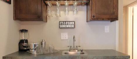 A kitchen with wooden cabinets, a built-in shelf with glasses, a coffee maker, and a sign on the wall.