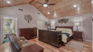 Un dormitorio con techo de madera, una cama, un aparador, una mesita de noche y un sofá.