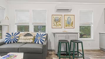 A modern living room with a gray sofa, two green stools, and a white kitchen area with a window.