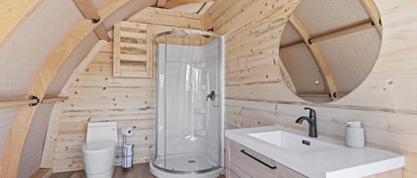A small, wooden cabin bathroom with a shower, toilet, and sink.