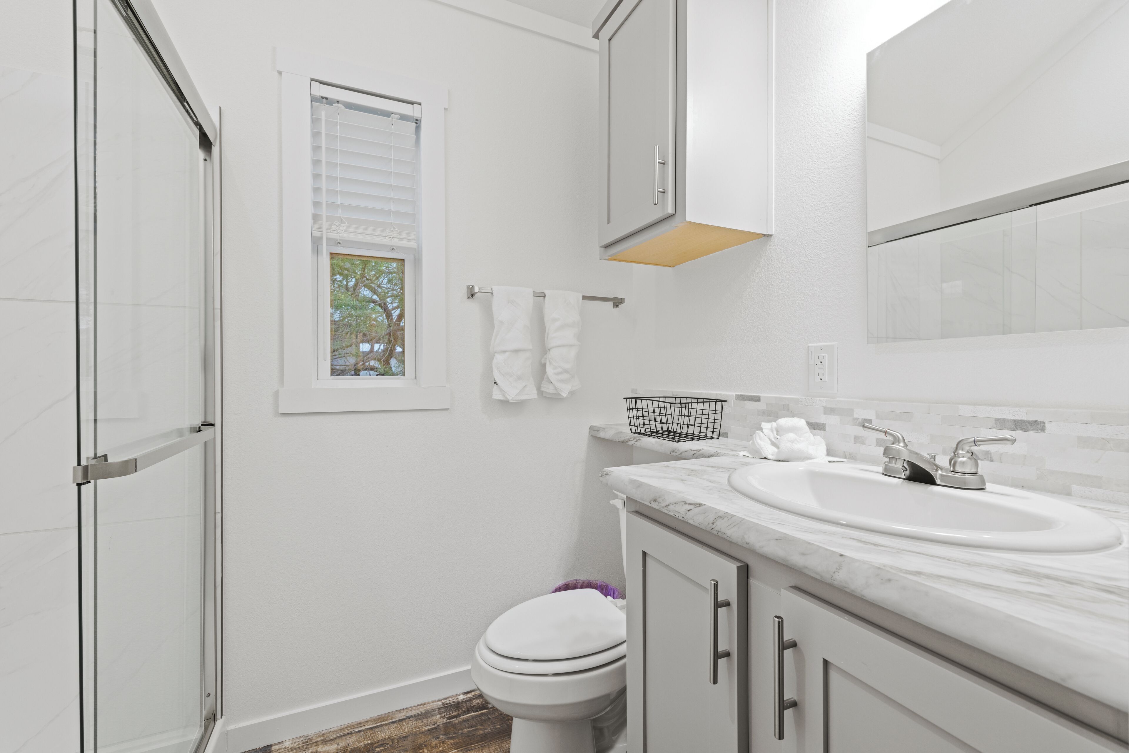 A bathroom with a white toilet, a sink with a marble countertop, and a shower area.