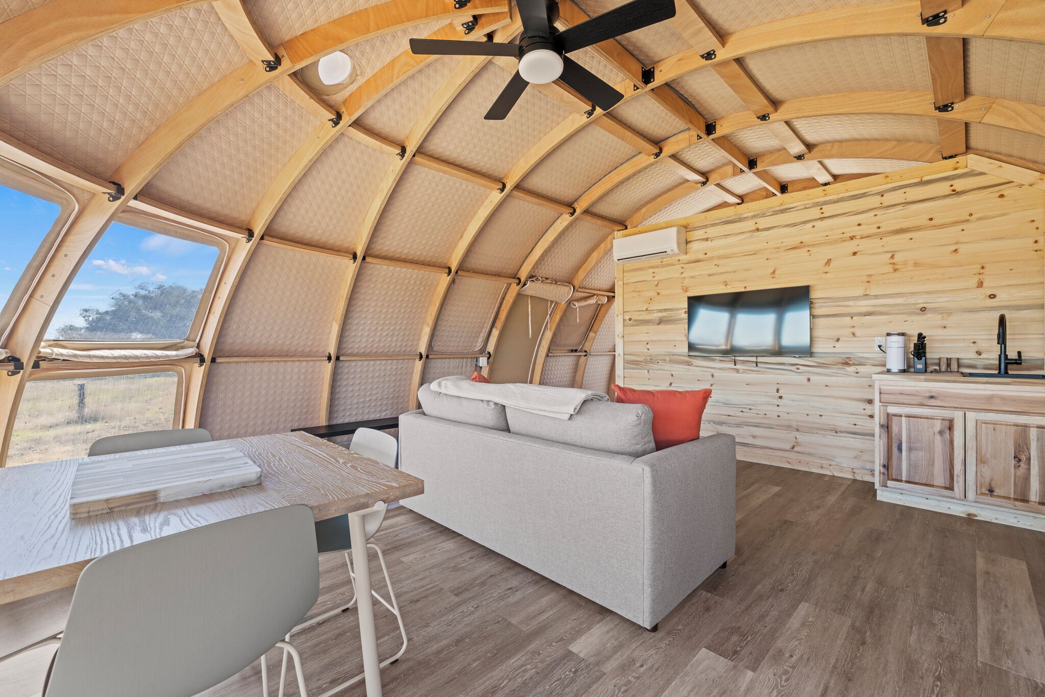 Un ambiente spazioso con soffitto in legno curvo, un divano, un tavolo da pranzo e un angolo cottura con mobili in legno e un televisore.