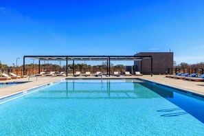 A swimming pool with sun loungers and a covered area, surrounded by a clear blue sky. - SKYE Texas Hill Country Resort  (Fredericksburg)