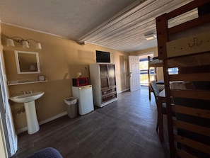 A compact kitchen with a sink, microwave, refrigerator, and a small trash bin.