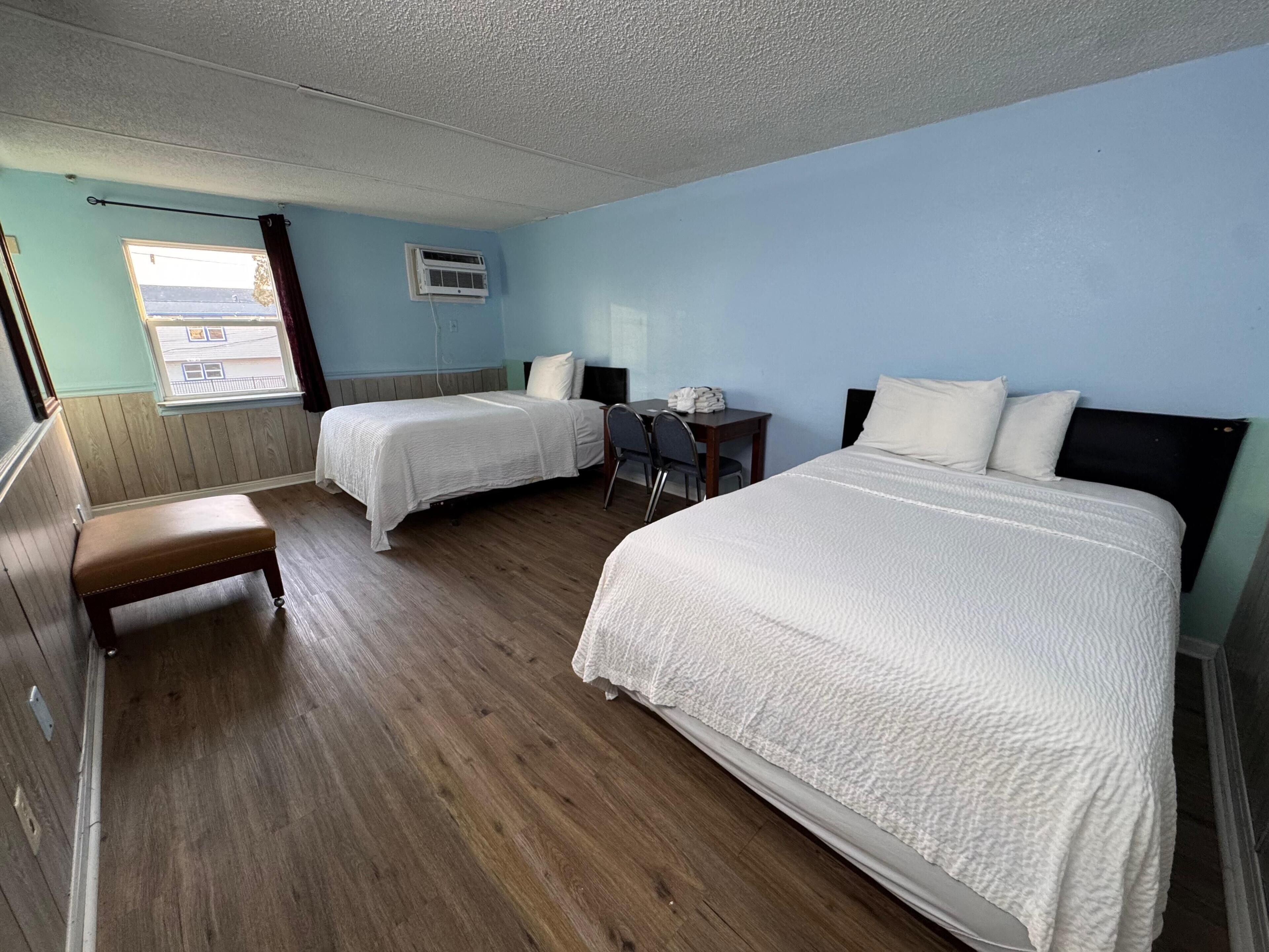 Une chambre d’hôtel avec deux lits, un bureau, une chaise, un banc et une fenêtre avec des rideaux.