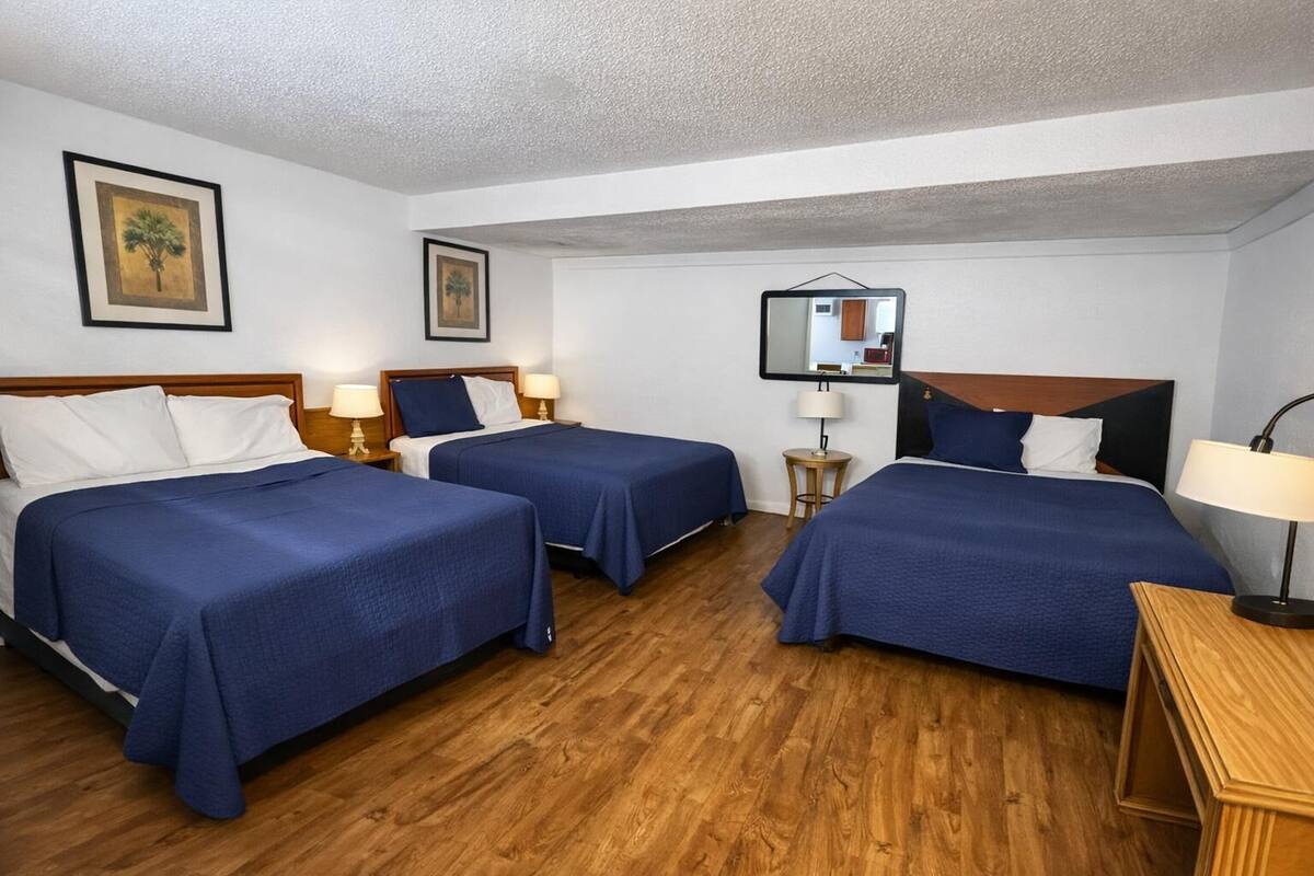 Habitación de hotel con dos camas, suelo de madera y una pequeña mesa con lámpara.