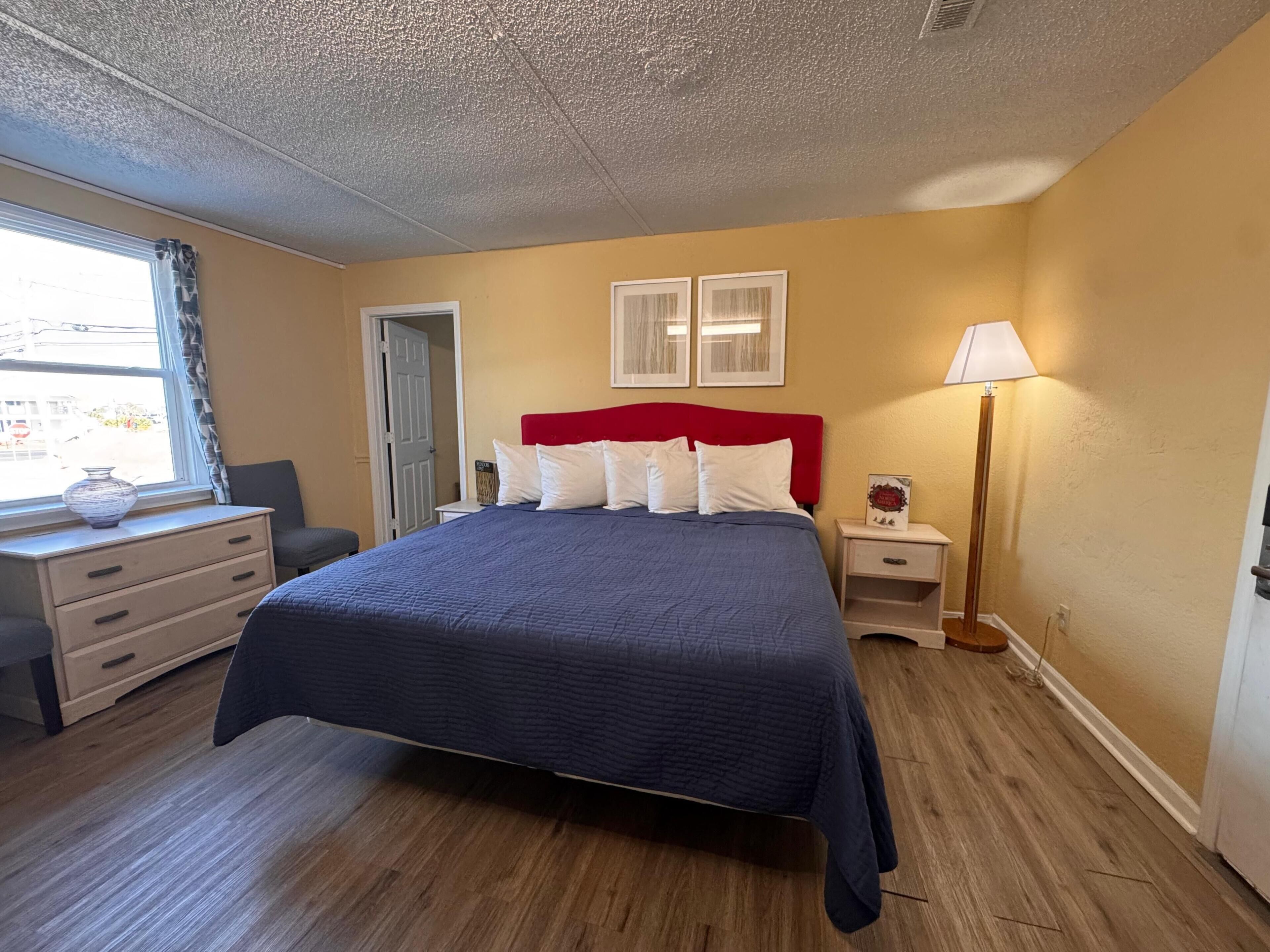 A bedroom with a bed, bedside tables, a lamp, a dresser, and a window with curtains.