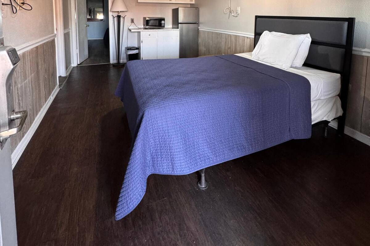 Un dormitorio con cama, televisor, kitchenette y puerta que da a otra habitación.