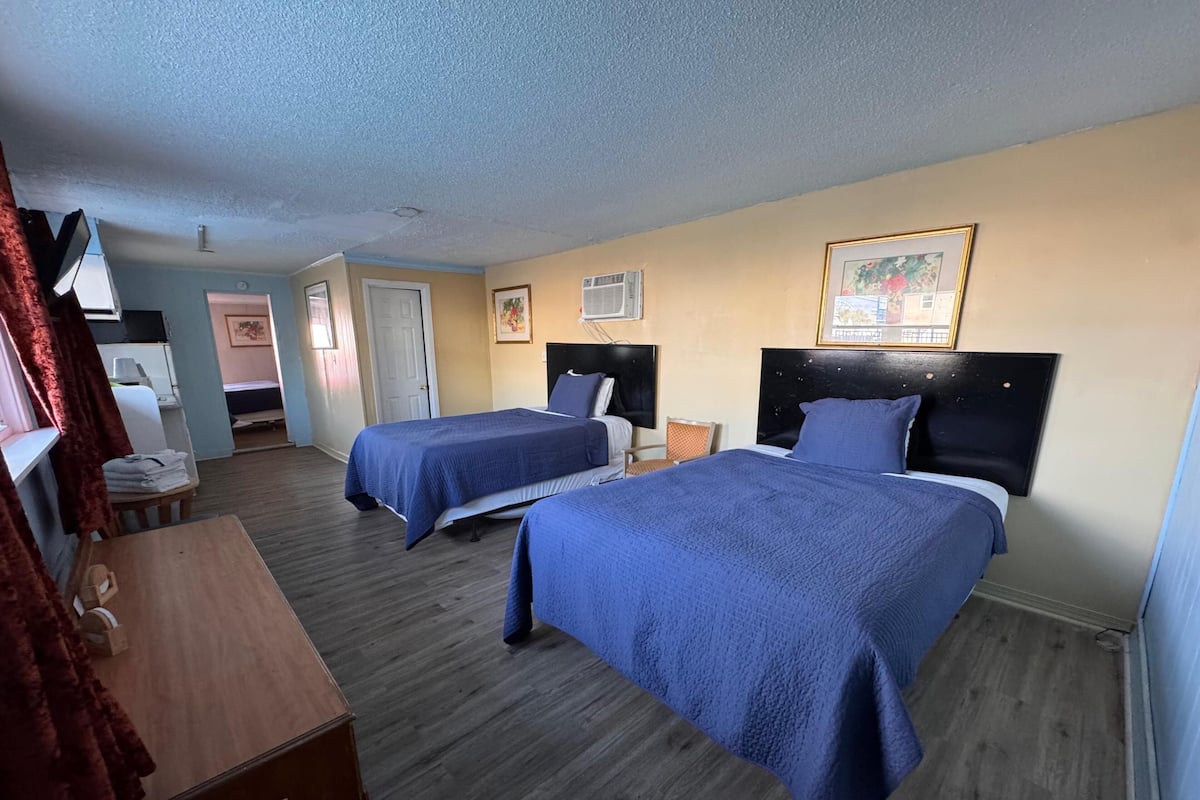 A hotel room with two beds, a wooden dresser, a desk, and a chair.