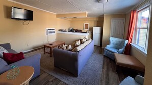 A living room with a sofa, a coffee table, a TV, a kitchen area, and a window with curtains. - CMI Hotel 1935 Myrtle Beach SC (Myrtle Beach)
