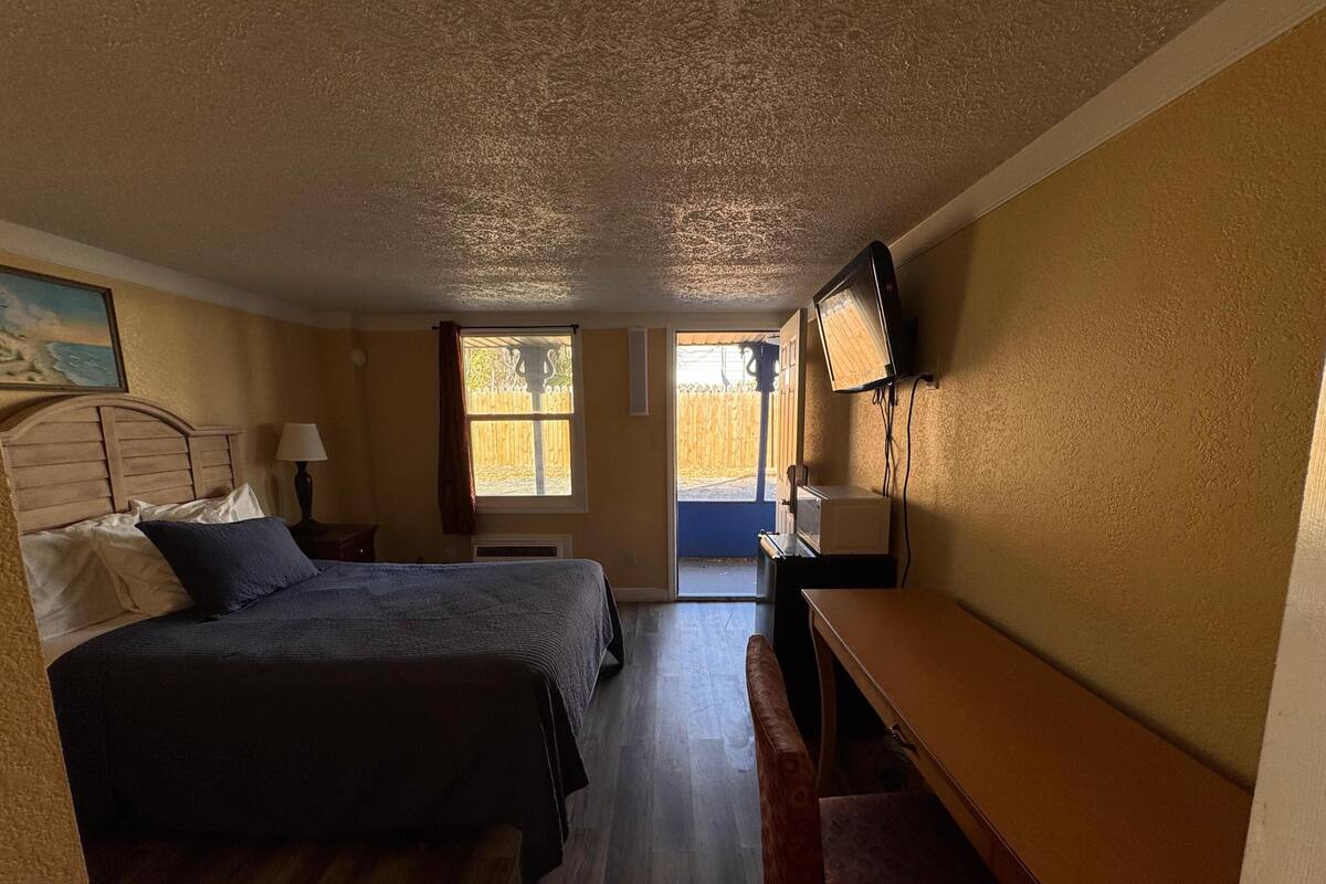 Un dormitorio con cama, mesita de noche, lámpara, televisor y escritorio.