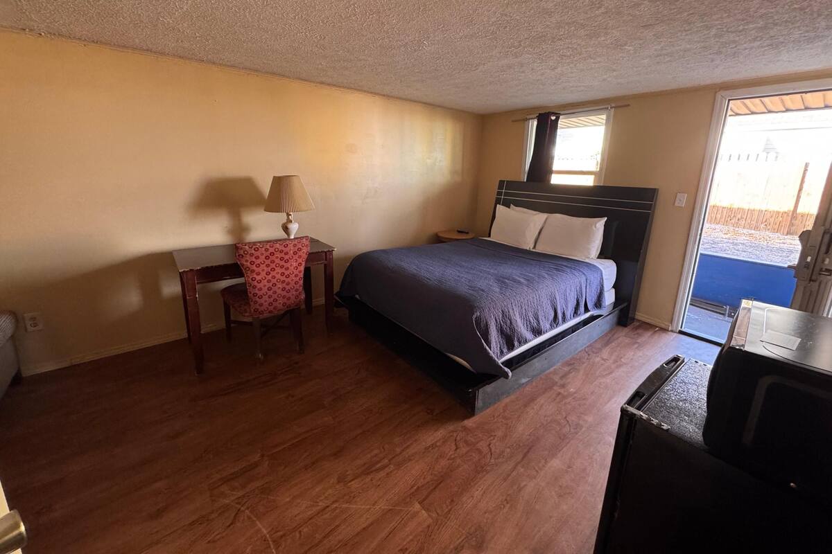 Un dormitorio con cama, escritorio con lámpara y vista al exterior.